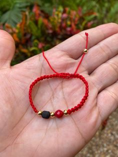 a hand holding a red string bracelet with black beads