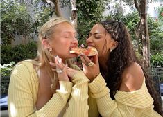 two beautiful young women sitting next to each other eating pizza