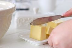 a person cutting cheese with a knife on a white plate next to a cup and saucer