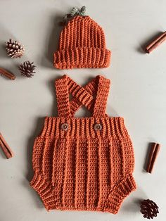 an orange knitted bodysuit and matching hat are on the table next to cinnamon sticks