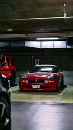 two cars parked in a parking garage next to each other on the street and one is red