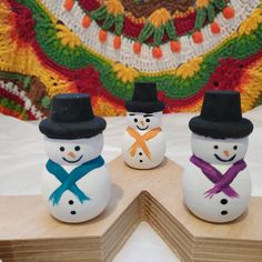 three snowmen sitting on top of a wooden block in front of a colorful blanket