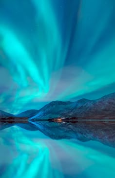 the aurora bore is reflected in water with mountains in the background and blue skies above