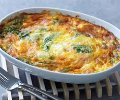 a casserole with cheese and spinach in a white dish next to silverware