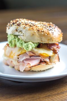 a sandwich with meat, cheese and guacamole on a white plate sitting on a wooden table