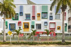 a multicolored building with palm trees in the foreground and a white fence around it