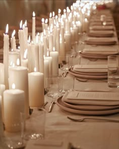 a long table is set with white candles and place settings for dinner guests to enjoy