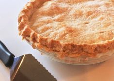 a pie sitting on top of a white table next to a knife and spatula