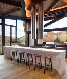 a kitchen with an island and four stools in front of the counter top that is surrounded by large windows