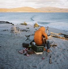 a man sitting on top of a sandy beach next to the ocean with a guitar