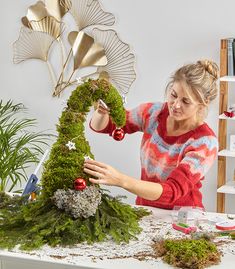 a woman is making a christmas tree out of moss and other decorations on a table