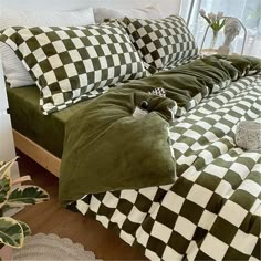 a bed covered in green and white checkered sheets next to a window with potted plants