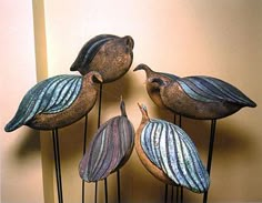 three metal birds sitting on top of each other next to a wall with a mirror behind them