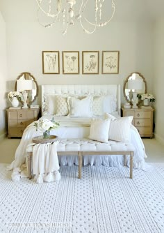 a white bed sitting under a chandelier in a bedroom next to two dressers