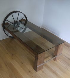 a glass table with a wooden wheel on top in front of a white wall and hardwood floor