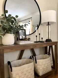 a mirror sitting above a wooden table with two baskets on it and a lamp next to it