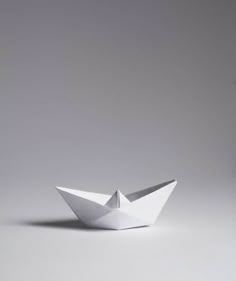 an origami boat is sitting on the floor in front of a gray background