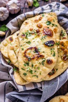 three pita breads with garlic and parsley on a cloth next to garlic cloves