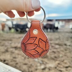 a hand holding a leather keychain in front of a herd of cows on a dirt field