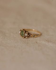 a gold ring with two green stones on the front and one stone in the back