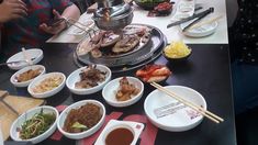 people sitting at a table with many plates of food in front of them, including meats and vegetables