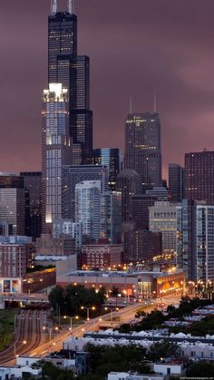 the city skyline is lit up at night, with skyscrapers in the background and cars parked on the street