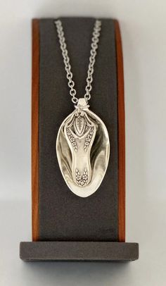 a silver necklace with an animal's head in the center on a wooden stand