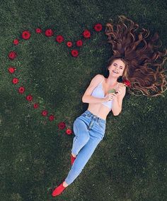 a woman laying in the grass with her hair blowing in the wind and flowers scattered around her