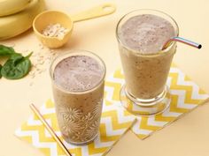 two glasses filled with smoothie sitting on top of yellow napkins next to bananas