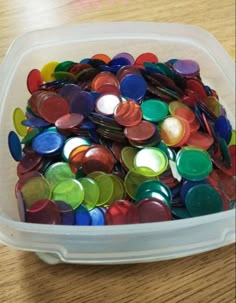 a plastic container filled with lots of different colored buttons on top of a wooden table