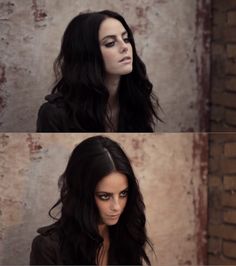 a woman with long black hair standing in front of a brick wall