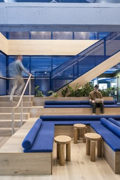 two men are walking up the stairs in an office building with blue couches and wooden stools