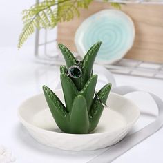 a white bowl filled with green plants on top of a table next to a plate