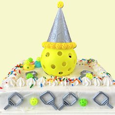 a yellow cake with white frosting and sprinkles has a party hat on top