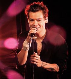 a man with tattoos on his arm holding a microphone and smiling at the camera while standing in front of bright lights