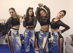 three women in shiny silver pants and black top posing for the camera with their arms behind them