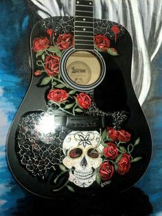 a black guitar with red roses and a skull painted on the front, sitting on a blue background