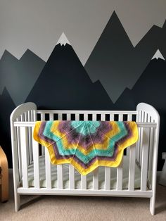 a crocheted blanket is draped over a white crib in front of mountains