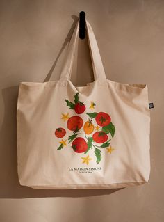 a white bag hanging on the wall with red flowers and leaves painted on it's side