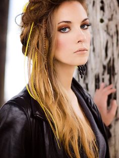 a woman with long hair standing in front of a tree wearing a black leather jacket