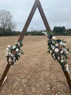 two wooden wedding archs decorated with flowers and greenery in the middle of a field