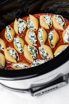 a crock pot filled with pasta and spinach covered in sauce on top of a white counter