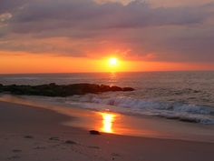 the sun is setting over the water at the beach