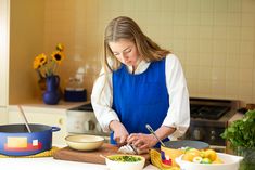 a woman in blue apron preparing food on cutting board next to pots and pans