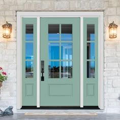 a green front door with two side lit lights and potted flowers on the porch