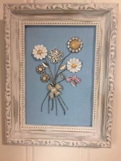 a white frame with flowers in it hanging on the wall next to a blue door