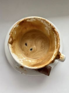 a white cup filled with brown liquid on top of a table next to a piece of chocolate