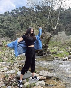 a woman standing on top of a rock next to a river