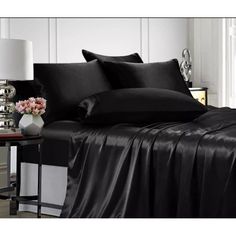 a bed with black sheets and pillows on top of it, next to a lamp