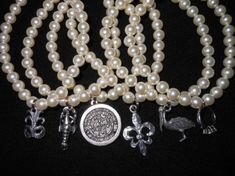 three necklaces with pearls and charms are shown on a black background, one has a silver charm